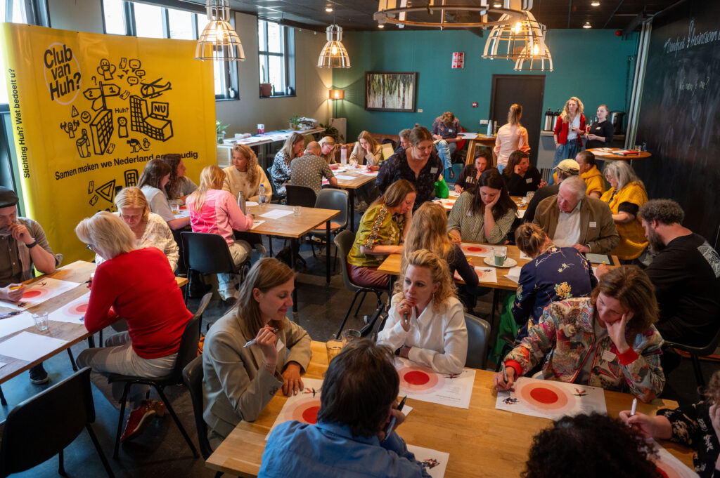Een workshopruimte vol met deelnemers die schrijven op gele notitieblaadjes. Het ziet er gezellig uit deze beweging.